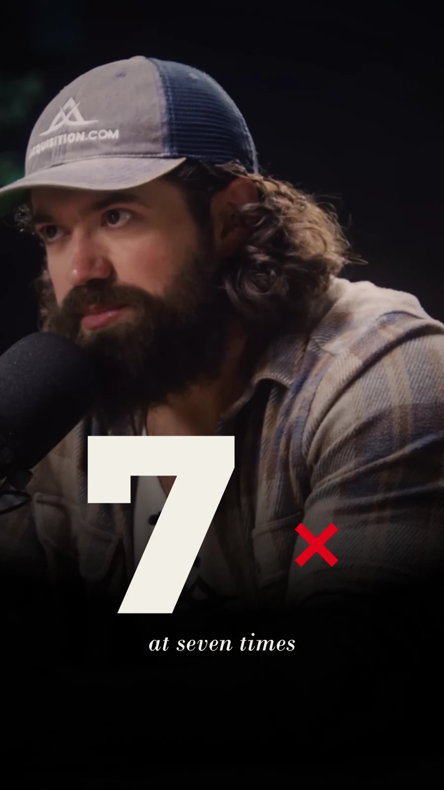 A speaker at a microphone above a large cream numeral 7 beside a red multiplication sign.